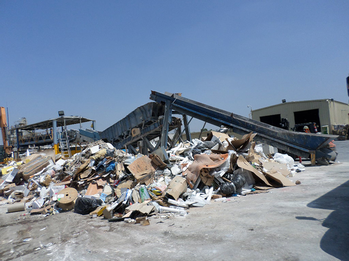 A crane at left scoops of refuse and dumps it on a conveyer belt where employees of Interior Removal Specialists remove items not suitable for recycling. Recyclable items come down the shoot and are retrieved by other workers. The South Gate firm has city permission to expand materials recycling operation in an enclosed structure to be built. (Photo by Arnold Adler)